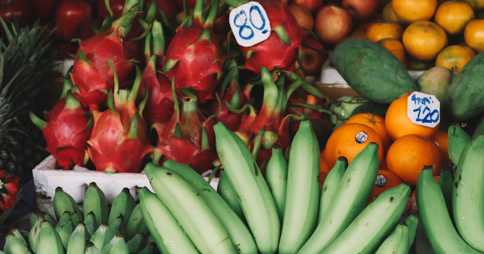 Dragon fruit, bananas and oranges with handwritten price tags on a market stall