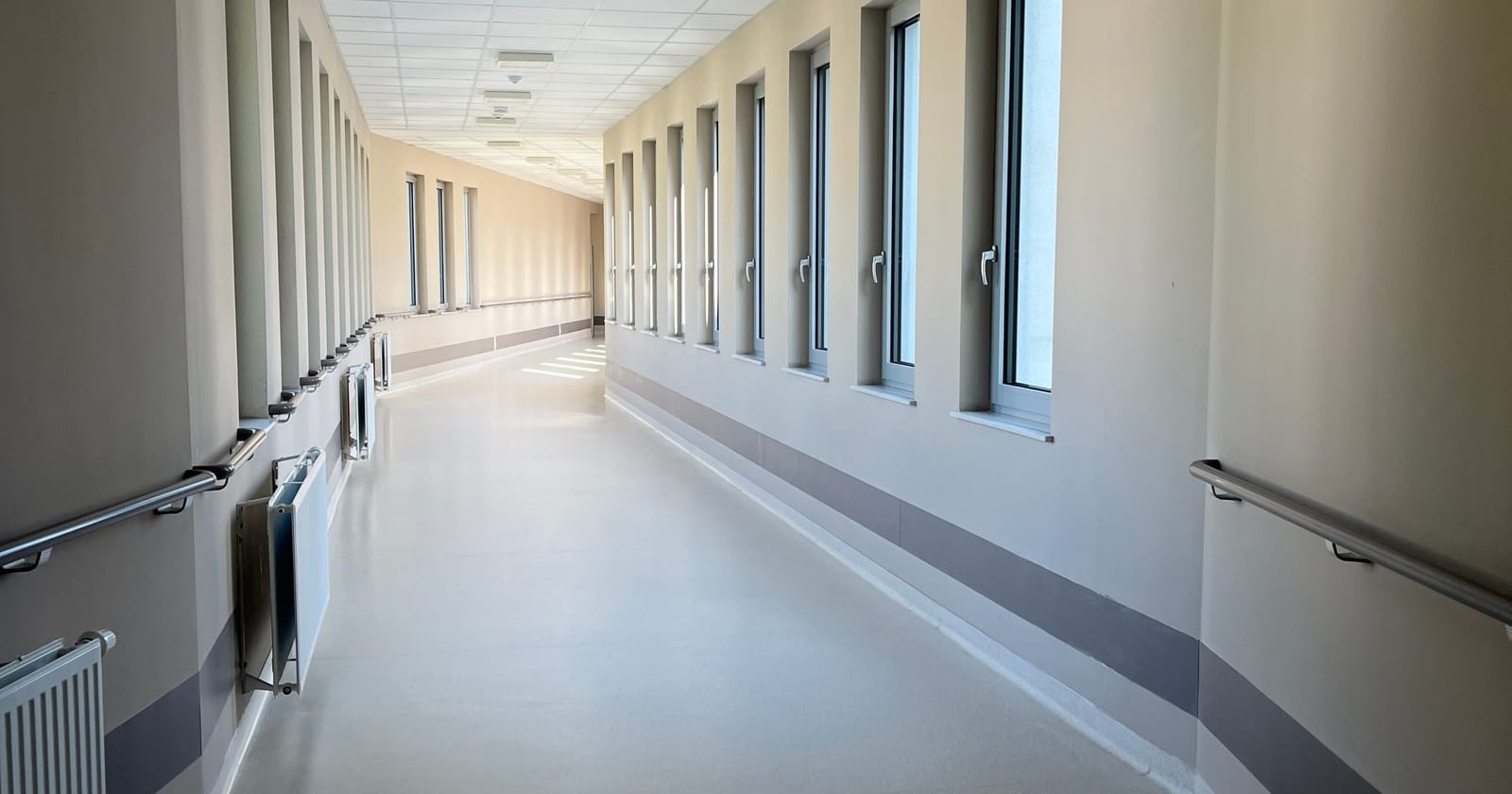 A bright, empty hospital corridor with handrails and tall windows