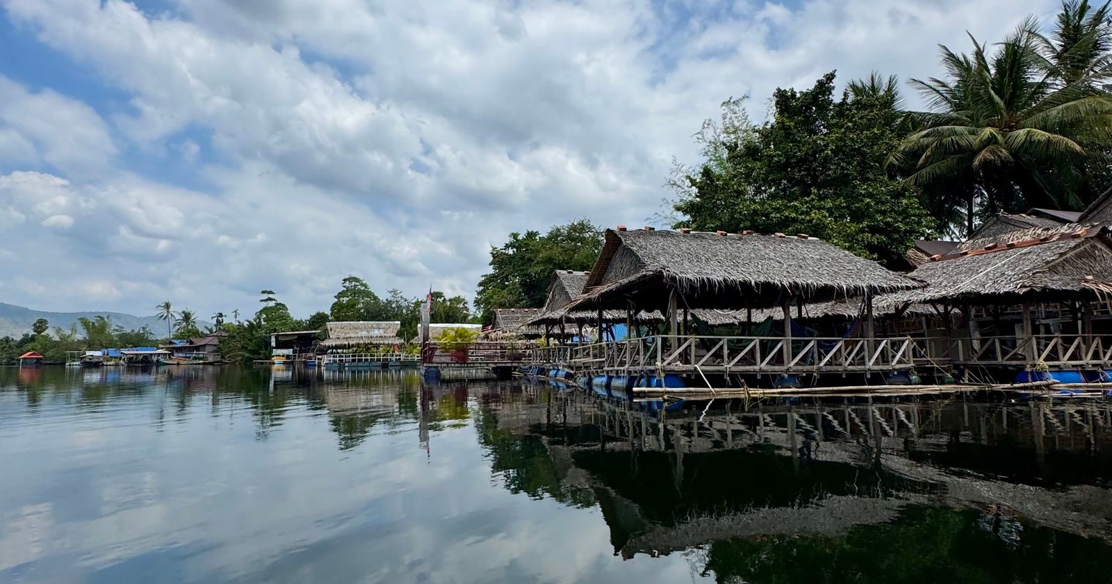 Thatched riverside huts on stilts reflected in the Kampot river
