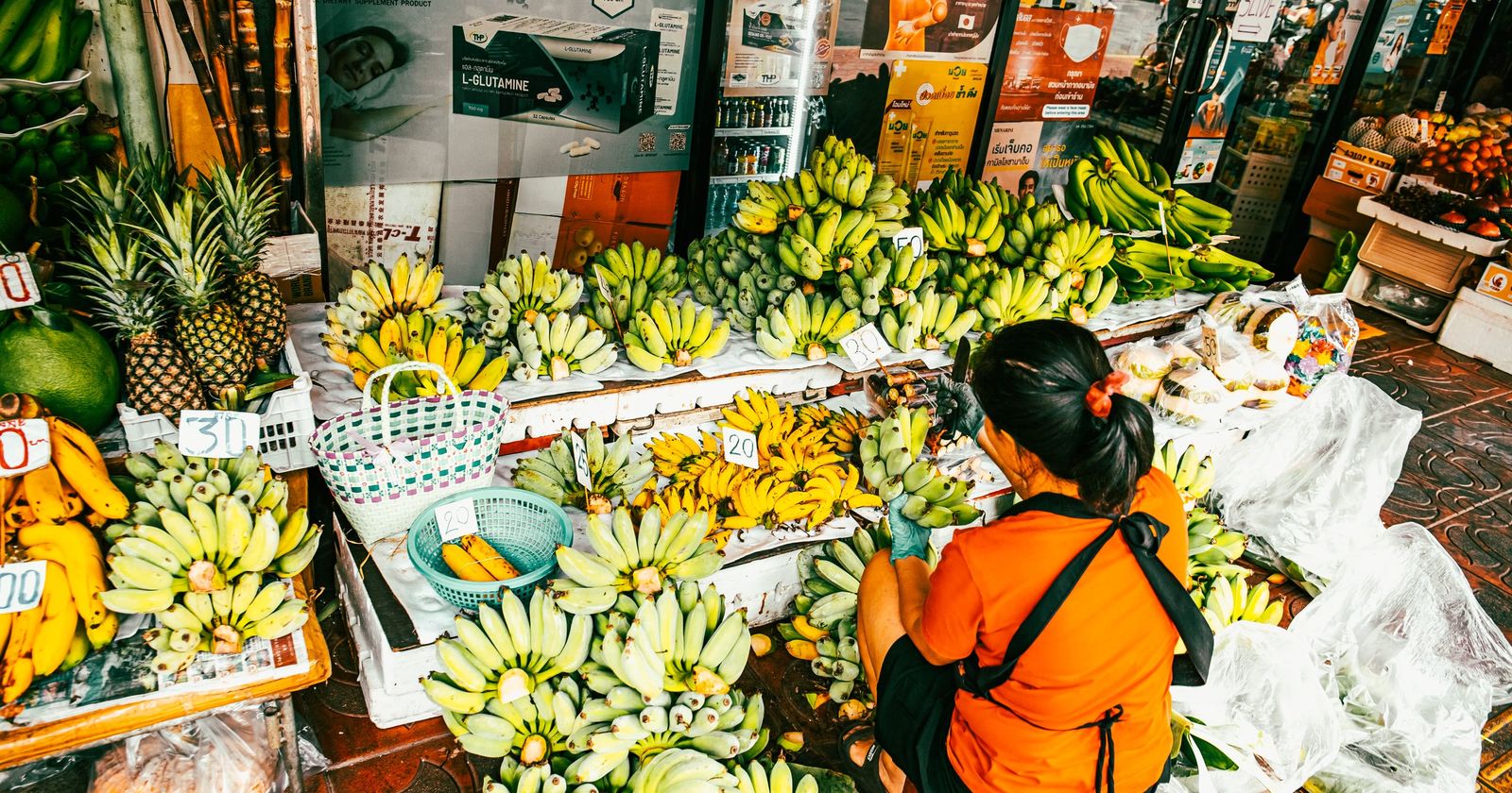 A stallholder arranging bananas and pineapples at a busy market