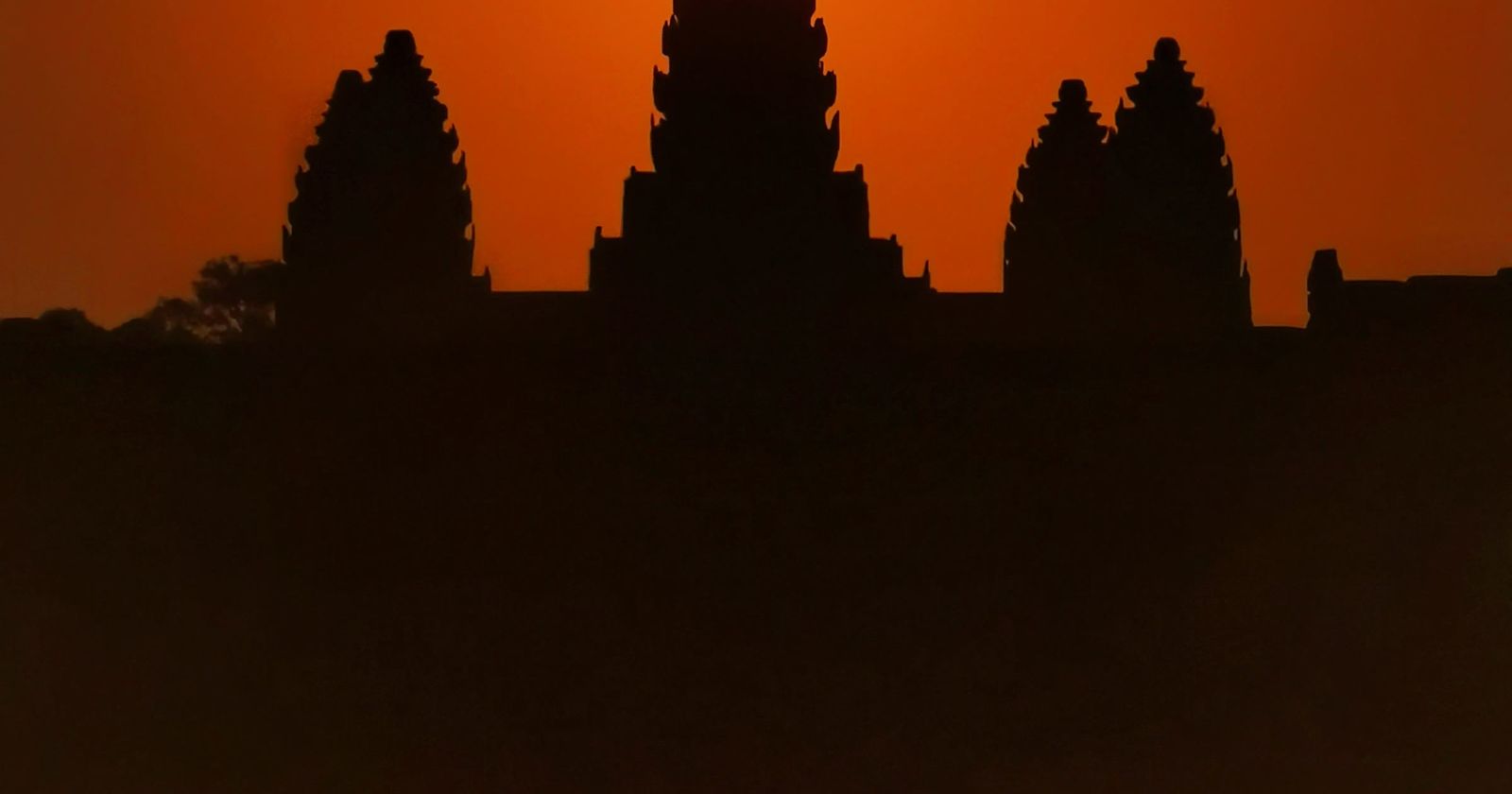The towers of Angkor Wat in silhouette against an orange sky