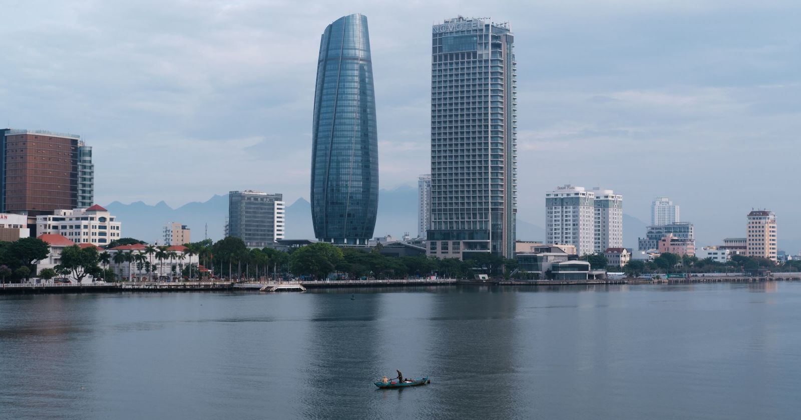 A riverside city in Vietnam with two tall towers and a small boat on the water