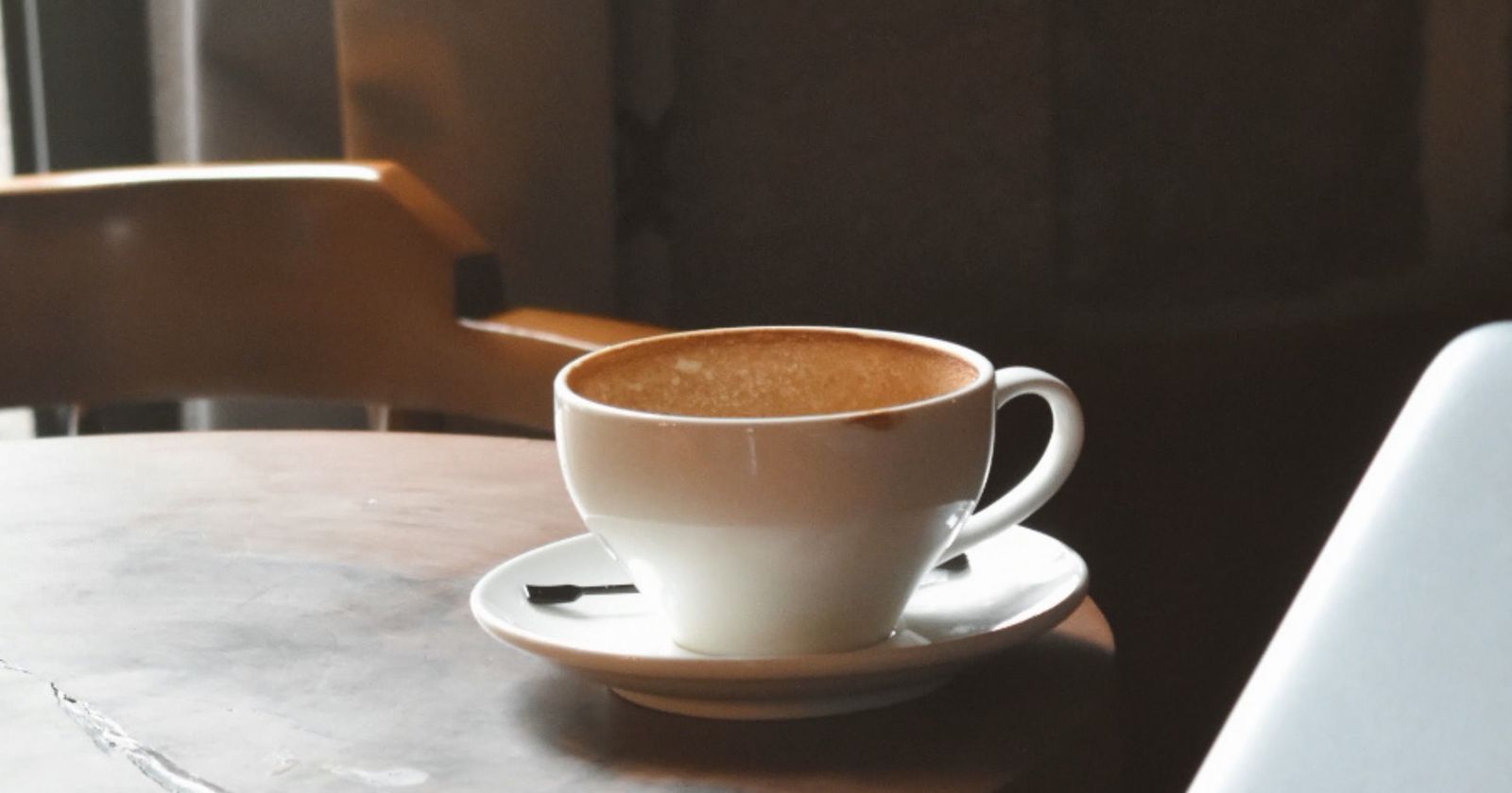 A cup of coffee on a café table next to a laptop
